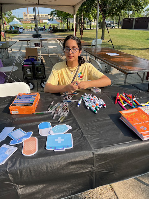 A young girl with dark hair and glasses sitting at a table with markers.